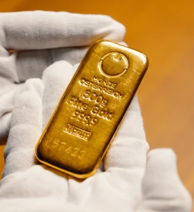 Ein Paar behandschuhte Hände, die einen 500-Gramm-Goldbarren mit der Aufschrift „Fine Gold 999.9“ halten.