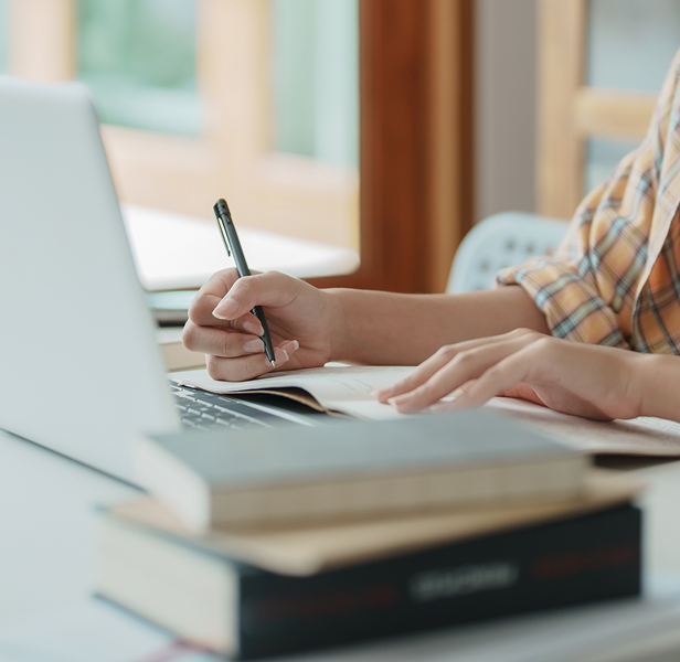 Frau macht sich Notizen, während sie online an Finanzkursen teilnimmt und Laptop sowie Notizbuch zu Hause nutzt