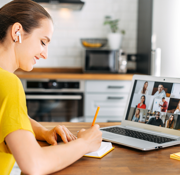 Frau nimmt an einem Finanz-Webinar am Laptop teil und macht sich Notizen während eines virtuellen Online-Kurses in der heimischen Küche